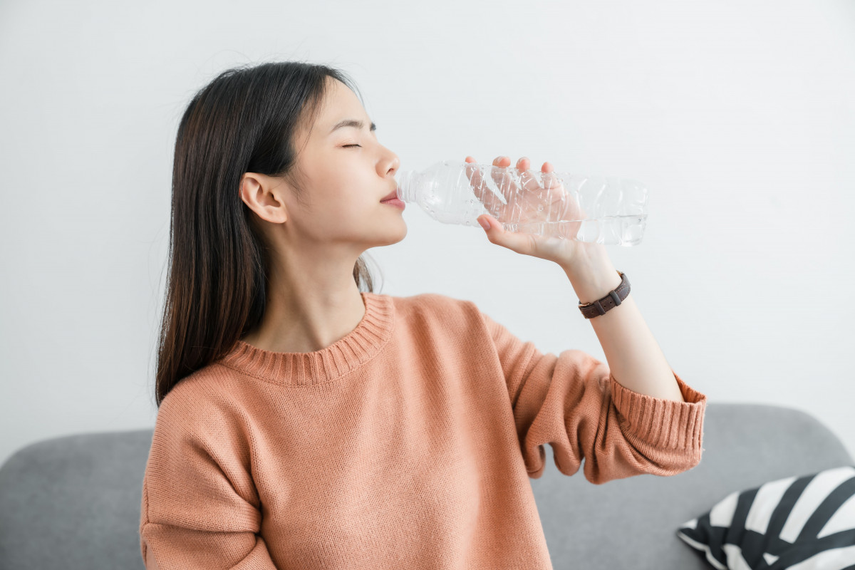 Seorang wanita sedang minum air putiih.