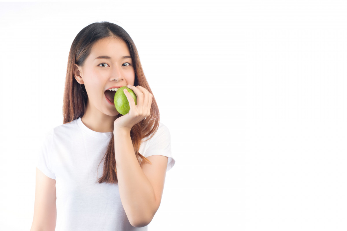 Seorang remaja perempuan sedang makan apel.