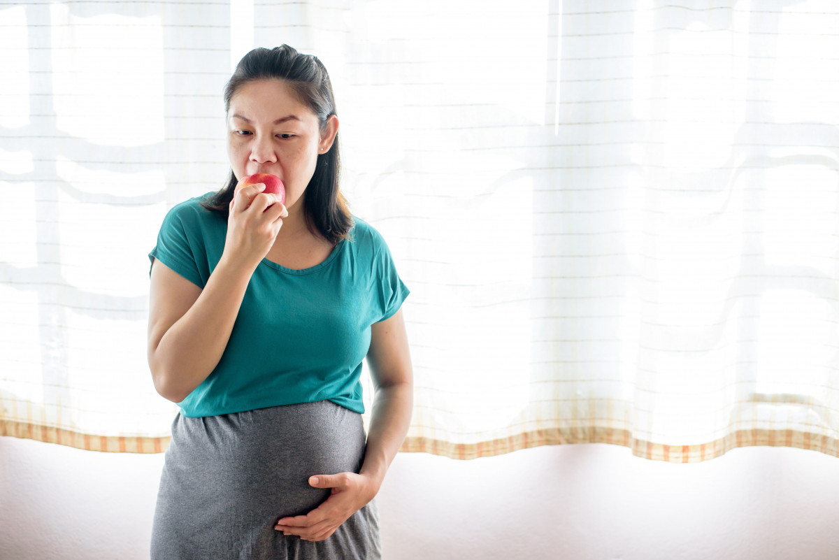 Wanita hamil sedang makan buah apel.
