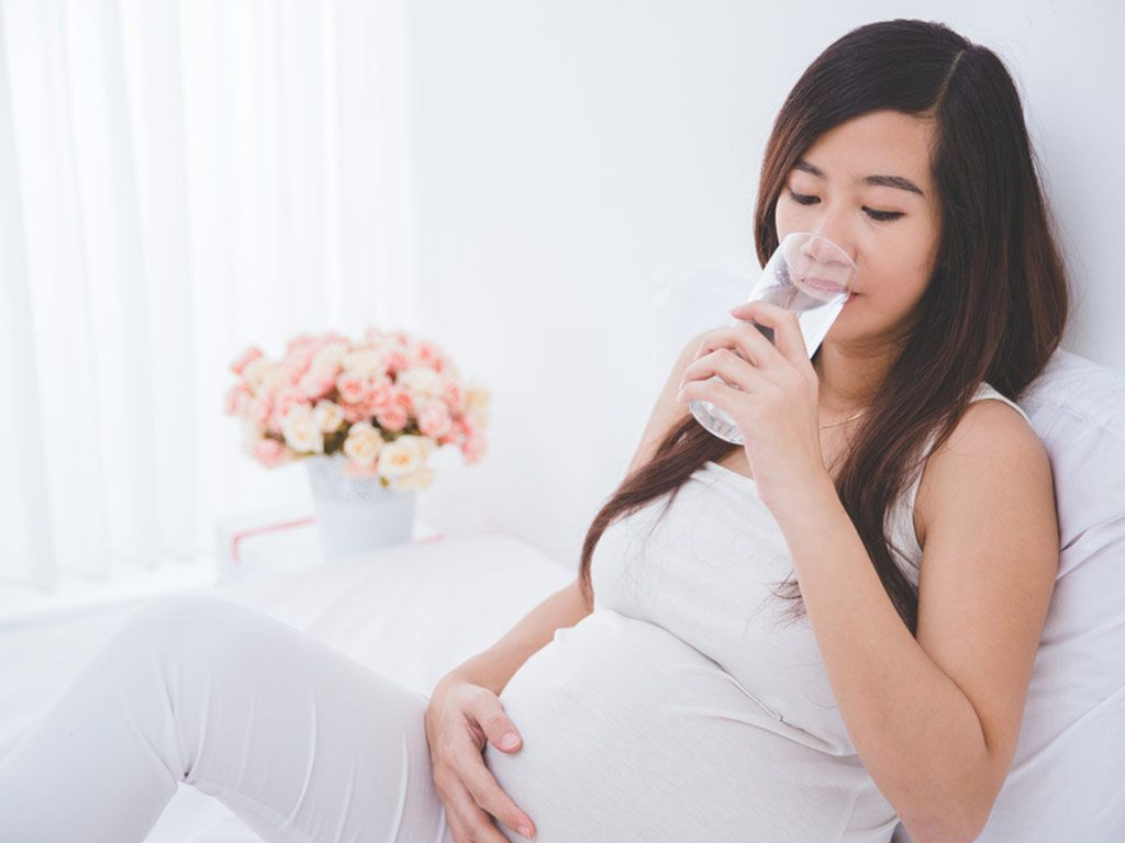 Wanita hamil sedang minum air.